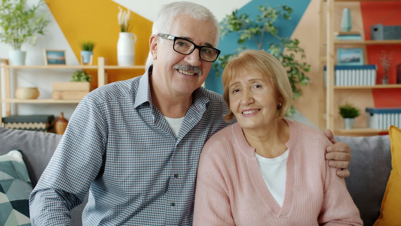 A couple in their seventies smiling on the couch