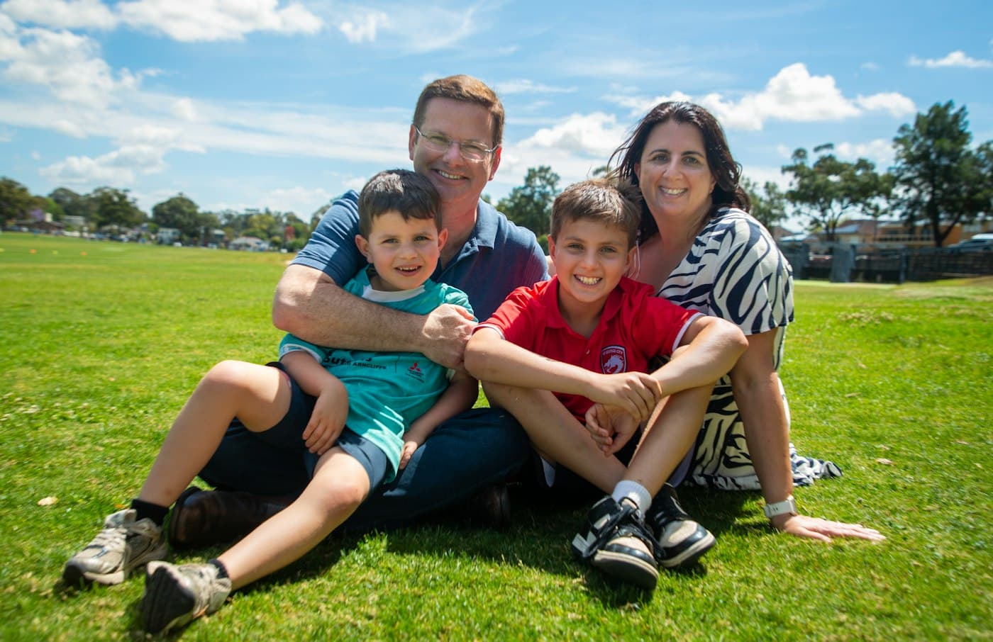 A family of four sitting together on the grass in a park