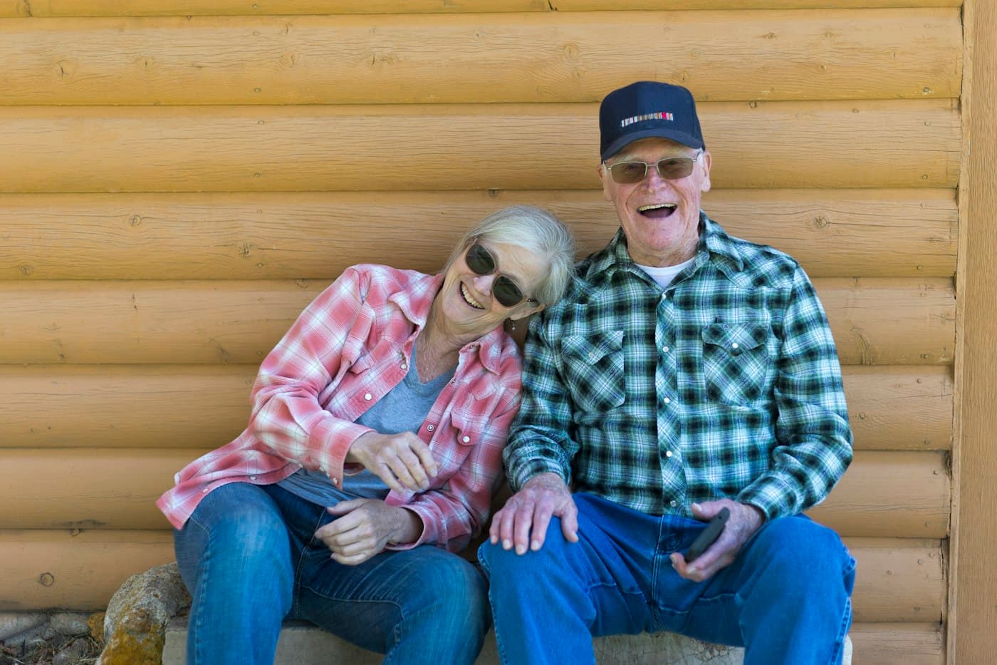 An older couple laughing together on a bench outside their home