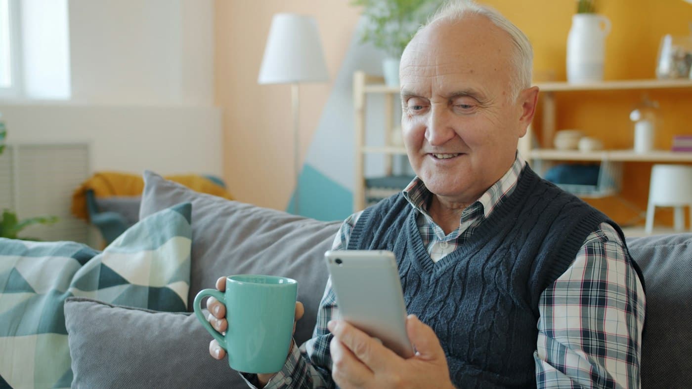 A man in his seventies reading his phone with a cup of coffee