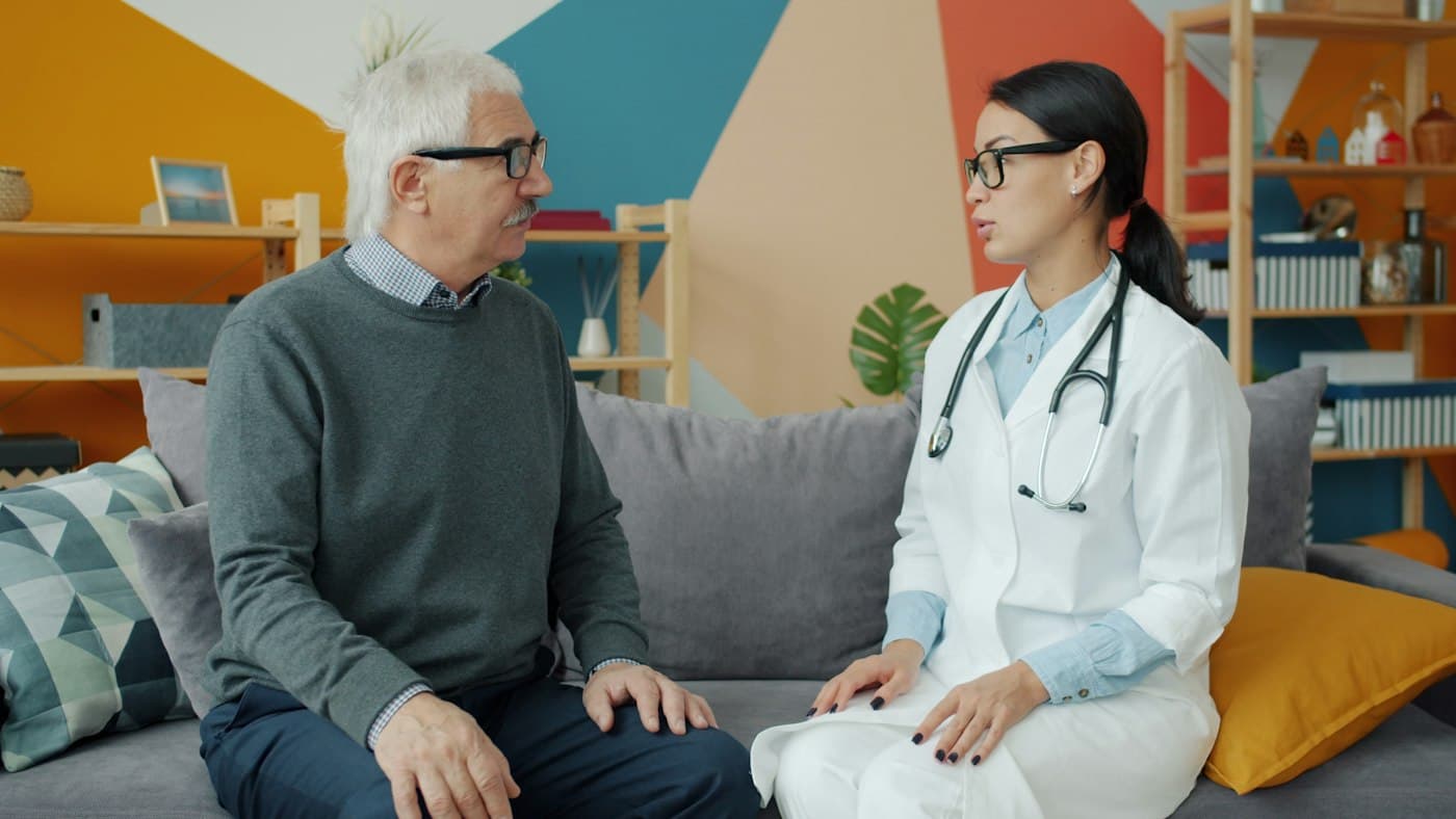 A doctor talking with an older man on his couch at home